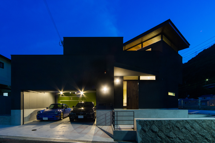 「神戸・灘区のガレージハウス」外観夜景。プライバシー確保のため、道路側には明かり取り用の窓のみ。2階のLDKはにはハイサイドライトがあり、屋根が浮いているように見せている