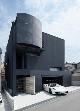 「東大阪のガレージハウス」外観を見る。四角いカタチの外観に、アール部分をデザインすることで、インパクトのある外観になった。コンクリート・タイル・スチールの各素材がバランス良く配されている