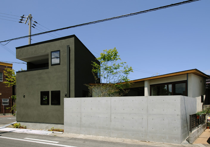 「岸和田・宮前町の中庭のある家・大阪」外観を見る。平屋と2階建ての2つの棟がある。平屋の方は土佐漆喰の壁にオーク材を貼った軒を持つ。2階棟は打ち合わせを重ねて決めたダークグリーンの左官仕上げ。 設計/藤原誠司 撮影/杉野圭