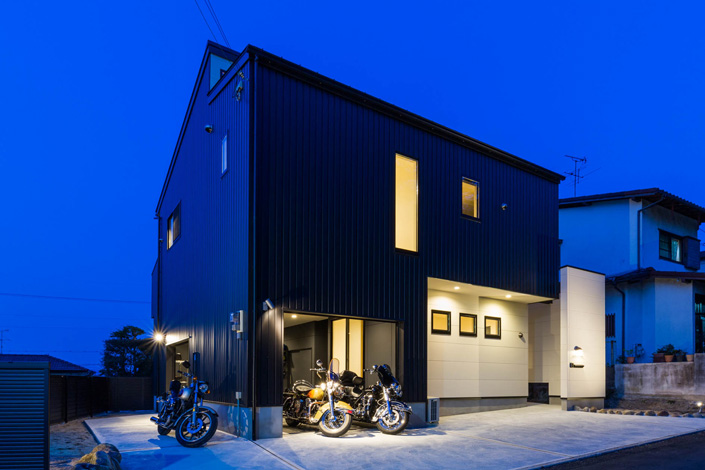 「王寺のガレージハウス・奈良」ガレージ夕景を見る。バイクの出し入れがしやすいようにガレージ側面にもシャッターが設けられている