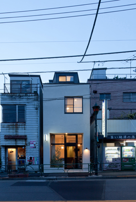 「根津の店舗併用住宅」通り越しに建物外観を見る（夜景）。両隣も店舗になっている。