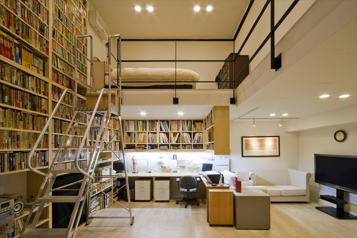 「本駒込の高級住宅・東京」地下にある書斎。吹抜けスペースを活かして、約3,000冊が収まる本棚に。正面は備え付けのデスク。右側には打合せスペース。ロフト部分にはベッドが置かれている。 設計／金富雄　撮影／平野和司